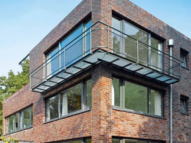 Corner of a brick townhouse with dark-framed Schueco CT 70 windows and a steel balcony