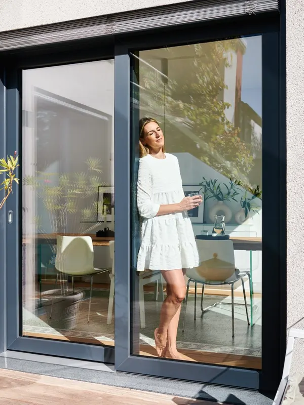 Woman standing in an open dark-framed Schueco EasySlide lift and slide door
